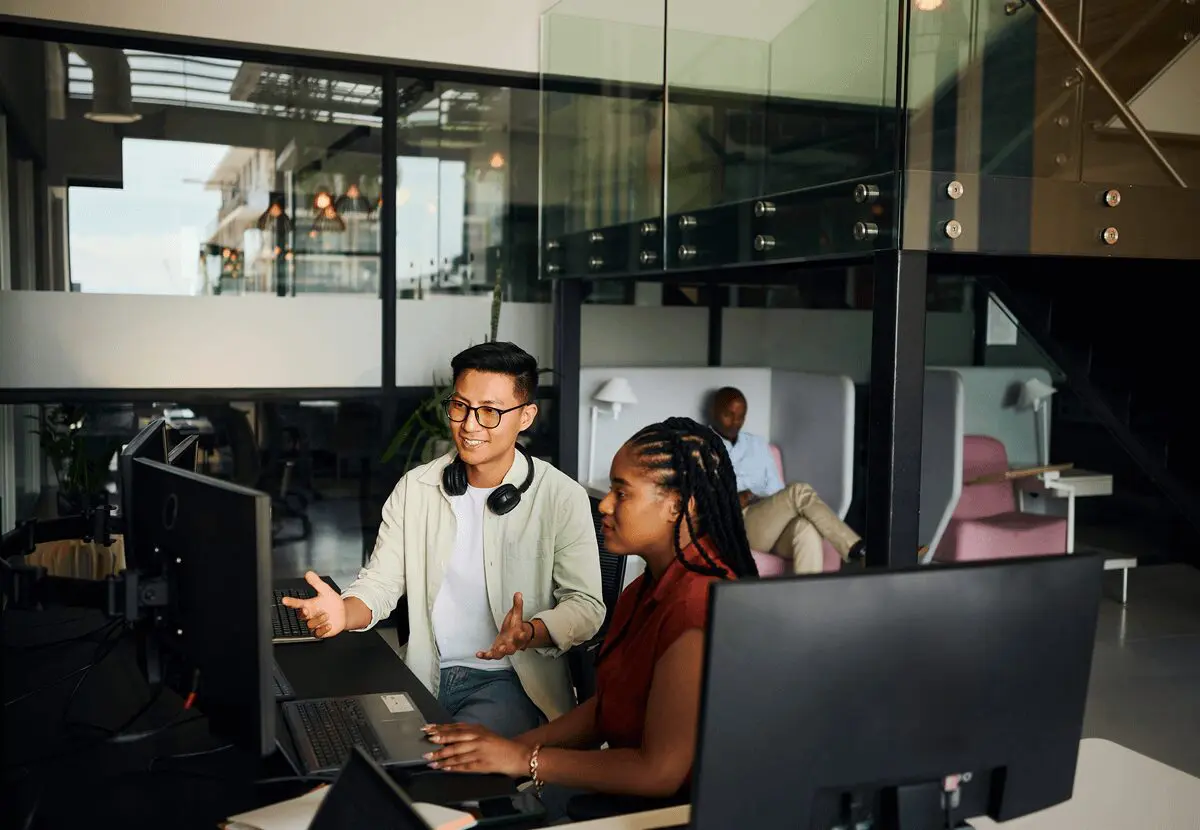 Colleagues collaborating at office computer desks.